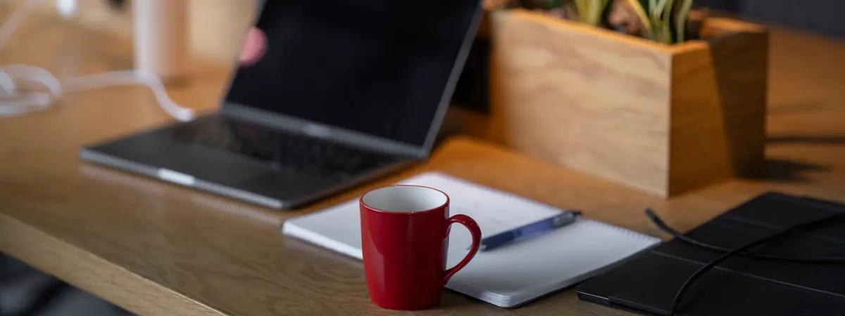 A laptop, a red mug and a notepad on a desk, the workspace of Best Criminal Justice Degree.