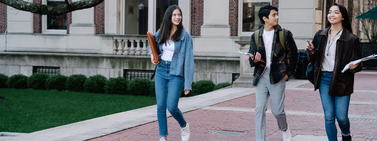 Three students walk past a stone building, a campus setting for a bachelor’s degree in criminal justice.