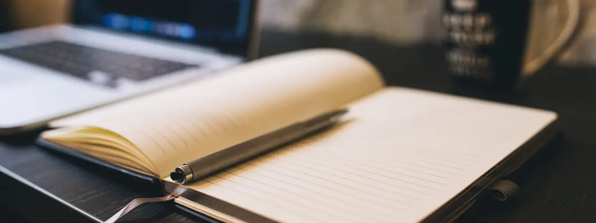 An open notebook with a pen beside a laptop, the desk behind a criminal justice degree blog.