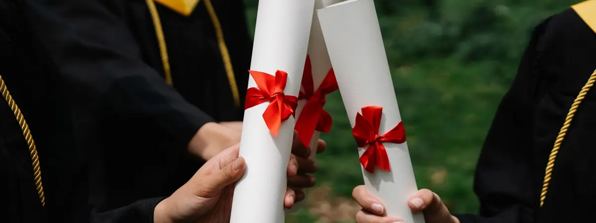 Hands hold rolled diplomas tied with red ribbons, the BA and BS degrees in criminal justice.