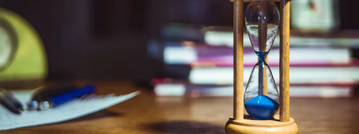 A wooden hourglass on a study desk beside books, timing how many years a criminal justice degree takes.