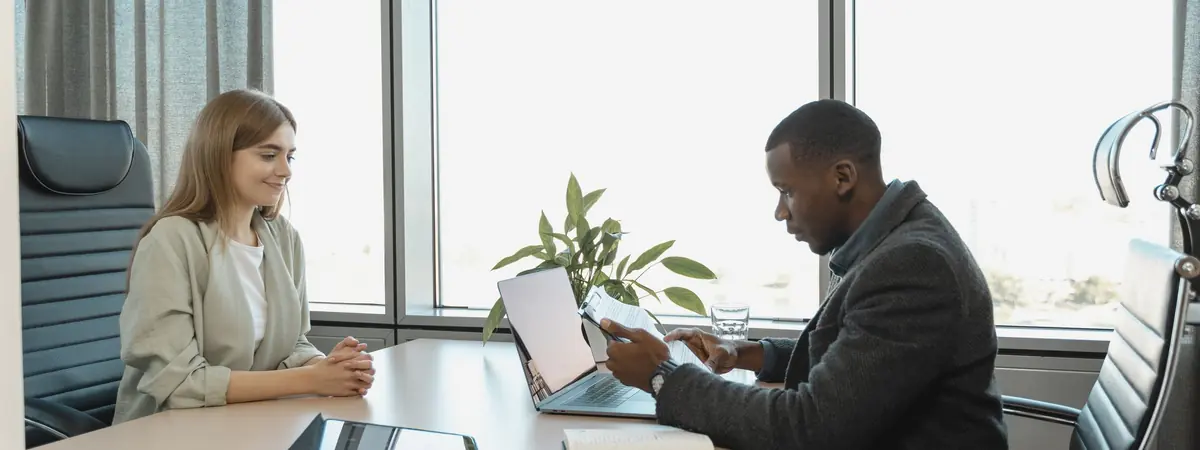 A man and a woman talk across a desk in a bright office, like a probation officer’s meeting.
