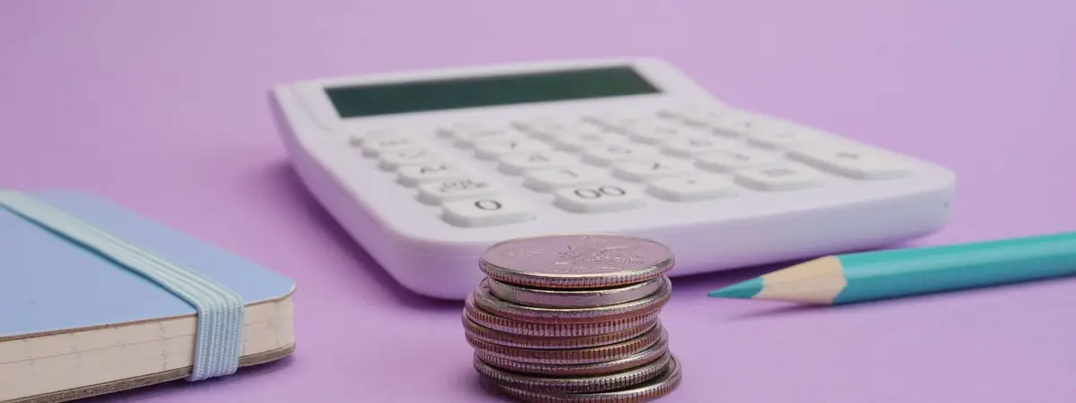 A calculator and a stack of coins on lavender, for pricing the cheapest online criminal justice degree.