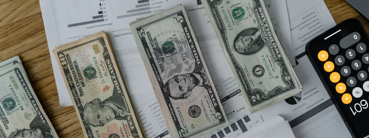 Dollar bills lie across printed charts beside a phone calculator, a look at criminal justice salary.