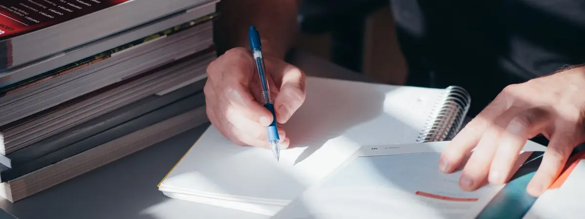 A person writes in a notebook beside stacked textbooks, weighing a degree to be a police officer.