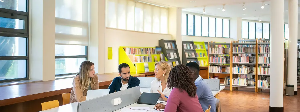 Graduate students compare notes around a shared table in a library, studying for a master’s in criminal justice.
