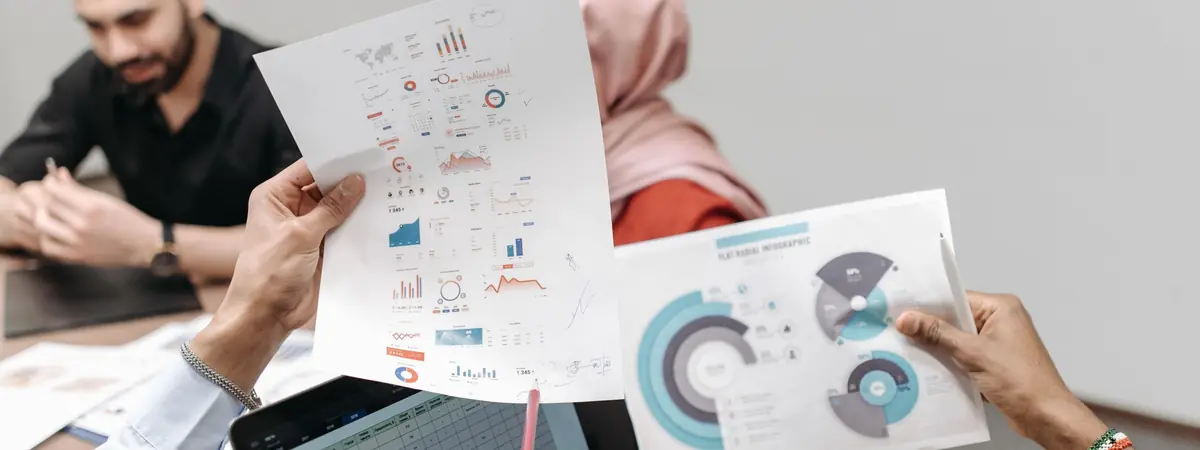 Colleagues compare printed charts beside a laptop showing a spreadsheet, the review behind ranking criminal justice programs.