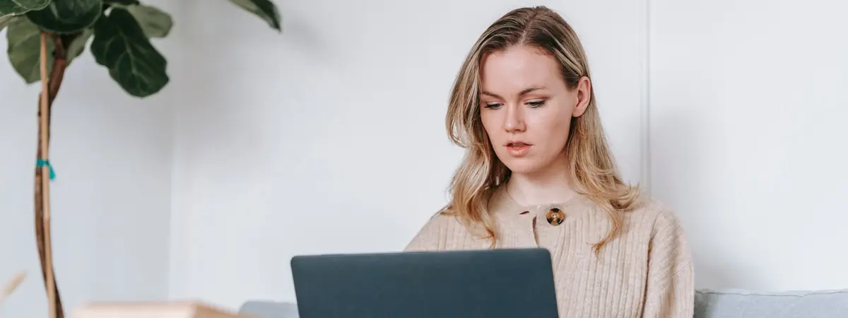 A woman works on a laptop in a bright room, studying for an online criminal justice degree.