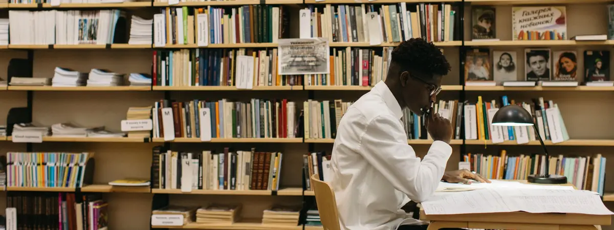 A researcher sits at a lamp-lit table among full bookshelves, working toward a PhD in criminal justice.