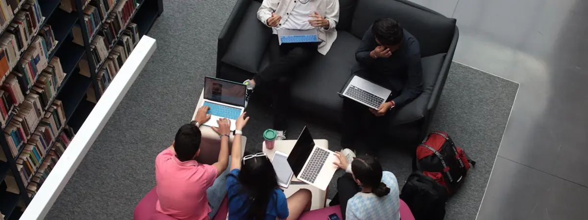 Five students study with laptops on sofas in a university library, a setting for criminal justice rankings.