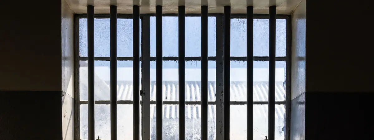 Daylight comes through a barred window in a dark cell wall, for an online corrections degree.