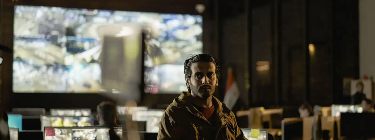 A man sits in a dim operations room with a wall of monitors, for a homeland security concentration.