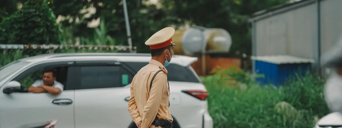 A traffic officer in a tan uniform stands beside a white car, for an online law enforcement degree.