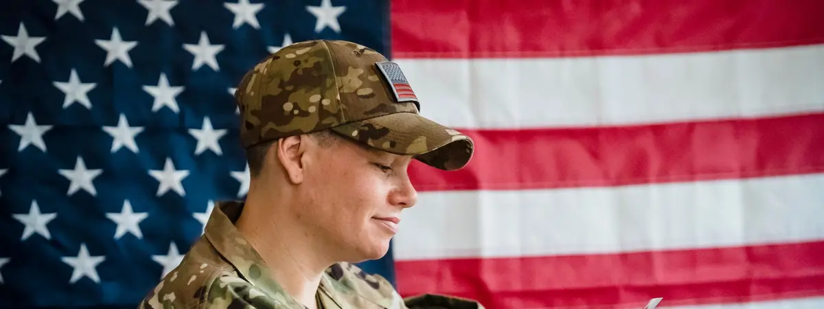A soldier reads at a table before an American flag, studying criminal justice degrees for military students.