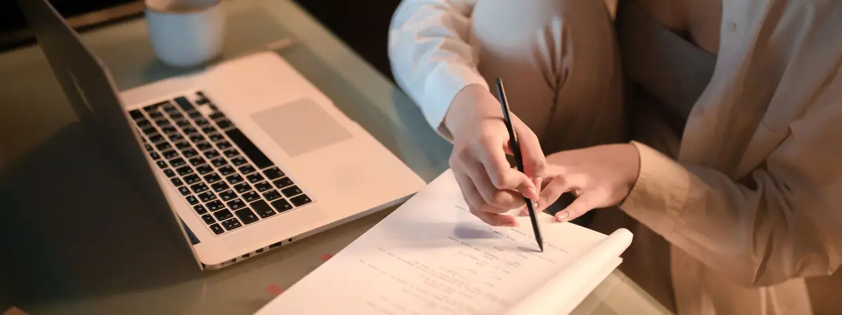 A hand takes notes with a pen beside a laptop, for criminal justice degrees for working adults.